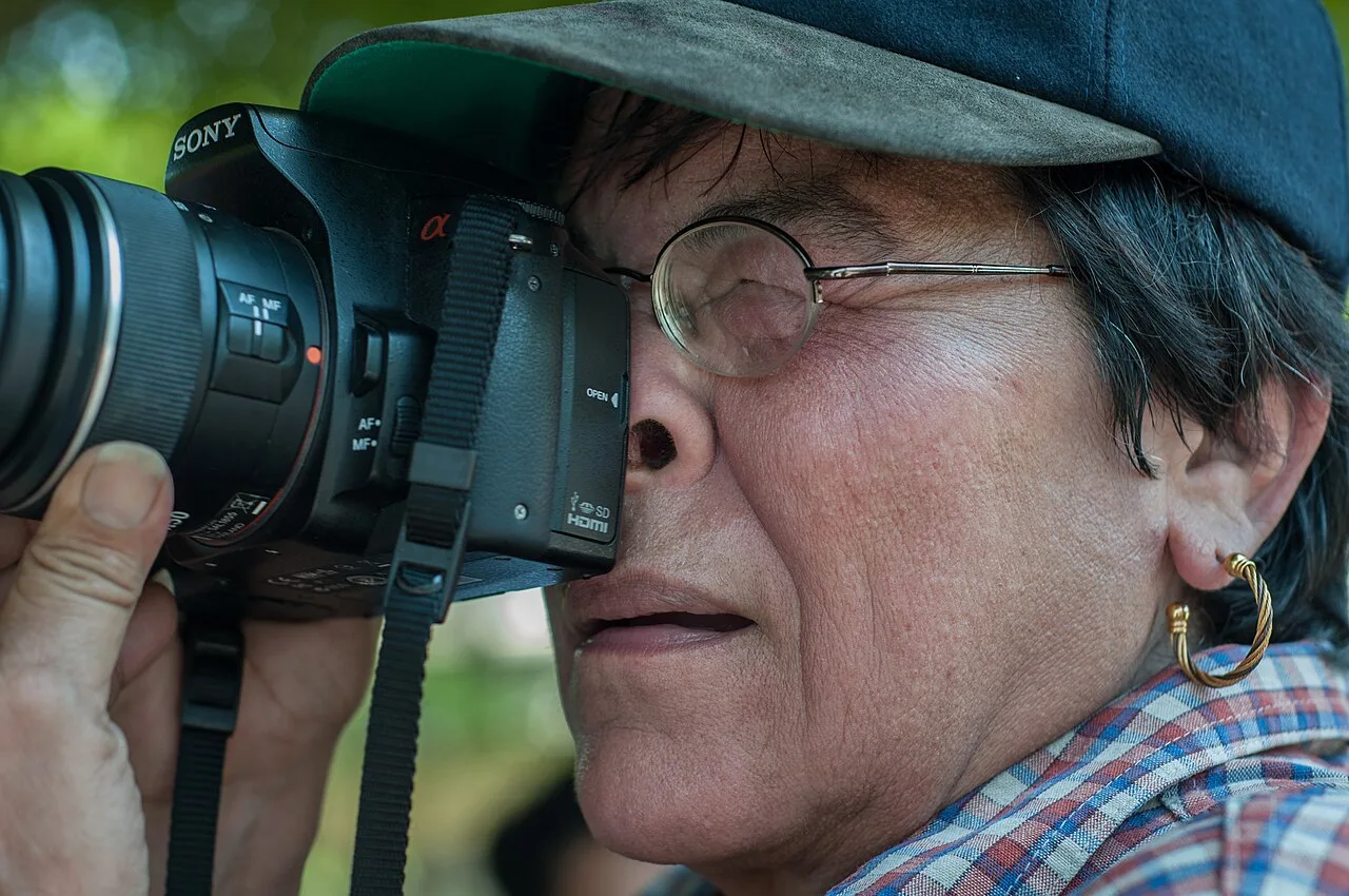 An Asian woman holding a camera outdoors