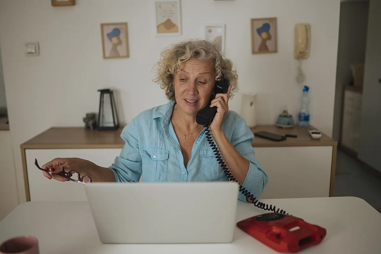 An adult woman using a laptop while speaking on a telephone at home